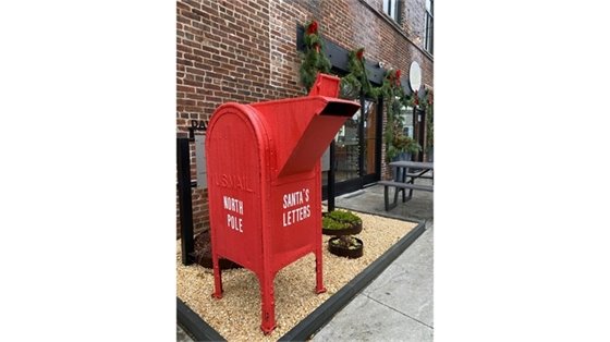 red santa mailbox outside brick building decorated with holiday greenery