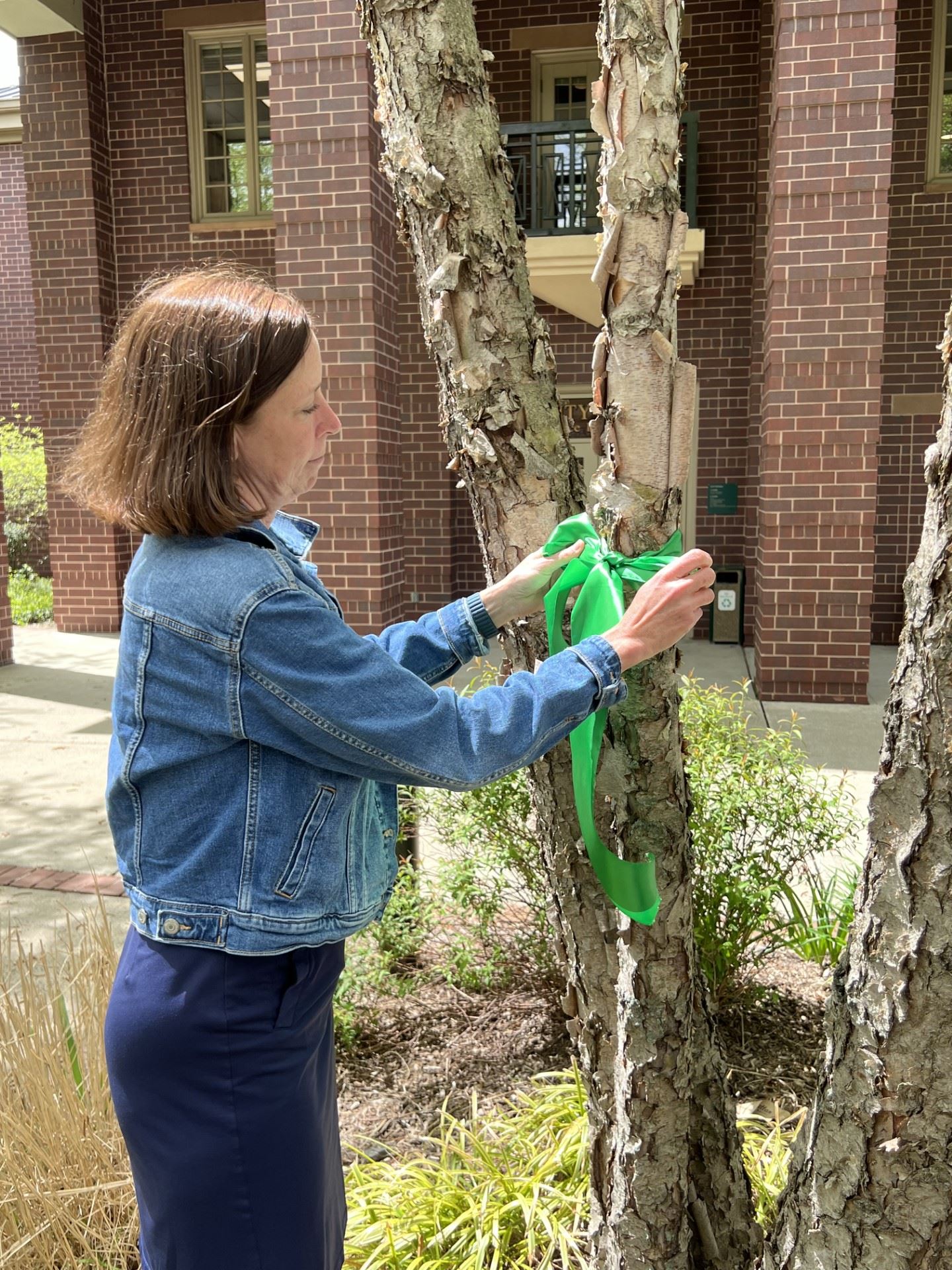person tying green ribbon around tree