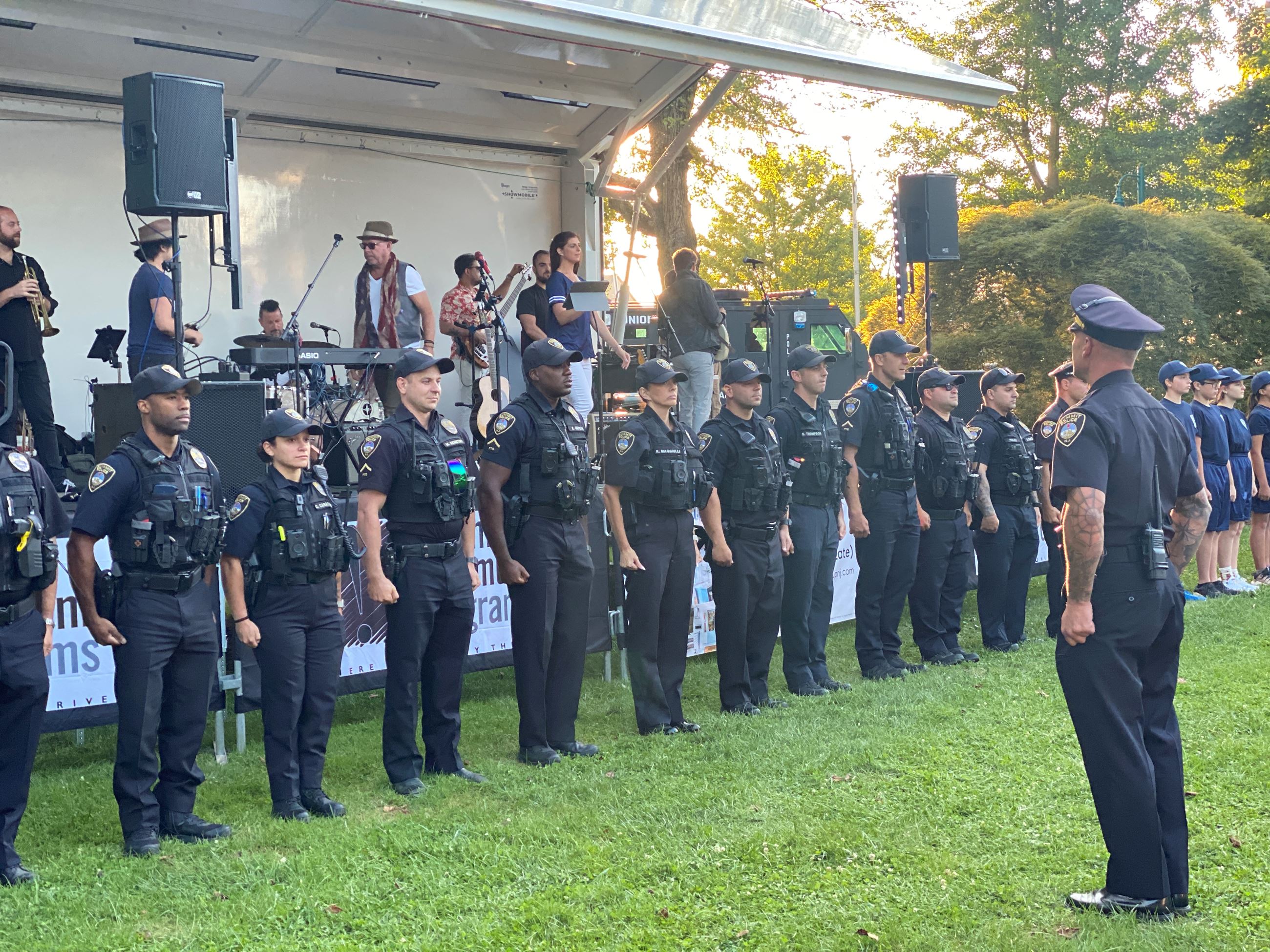 Police officers in a line in front of a stage in grassy park area