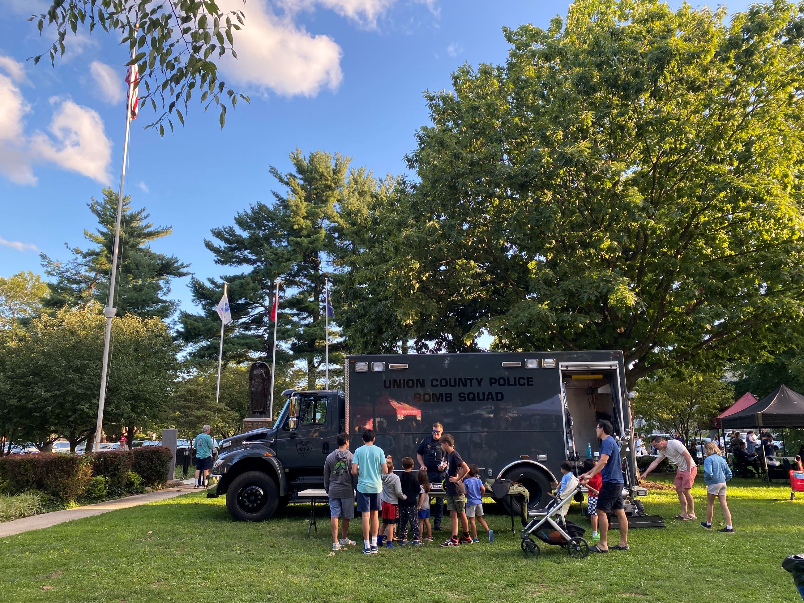 Large gray truck with people in front of it on grassy park area