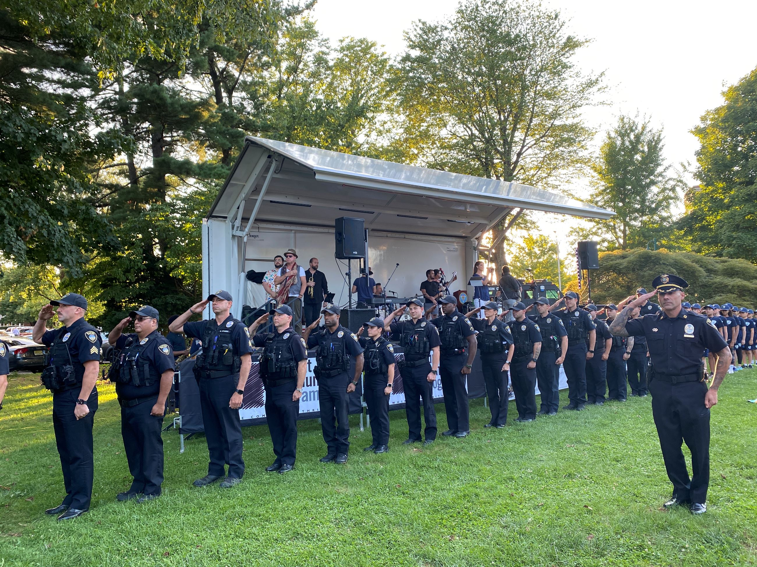 Police officers in salute in a line in front of a stage in grassy park area