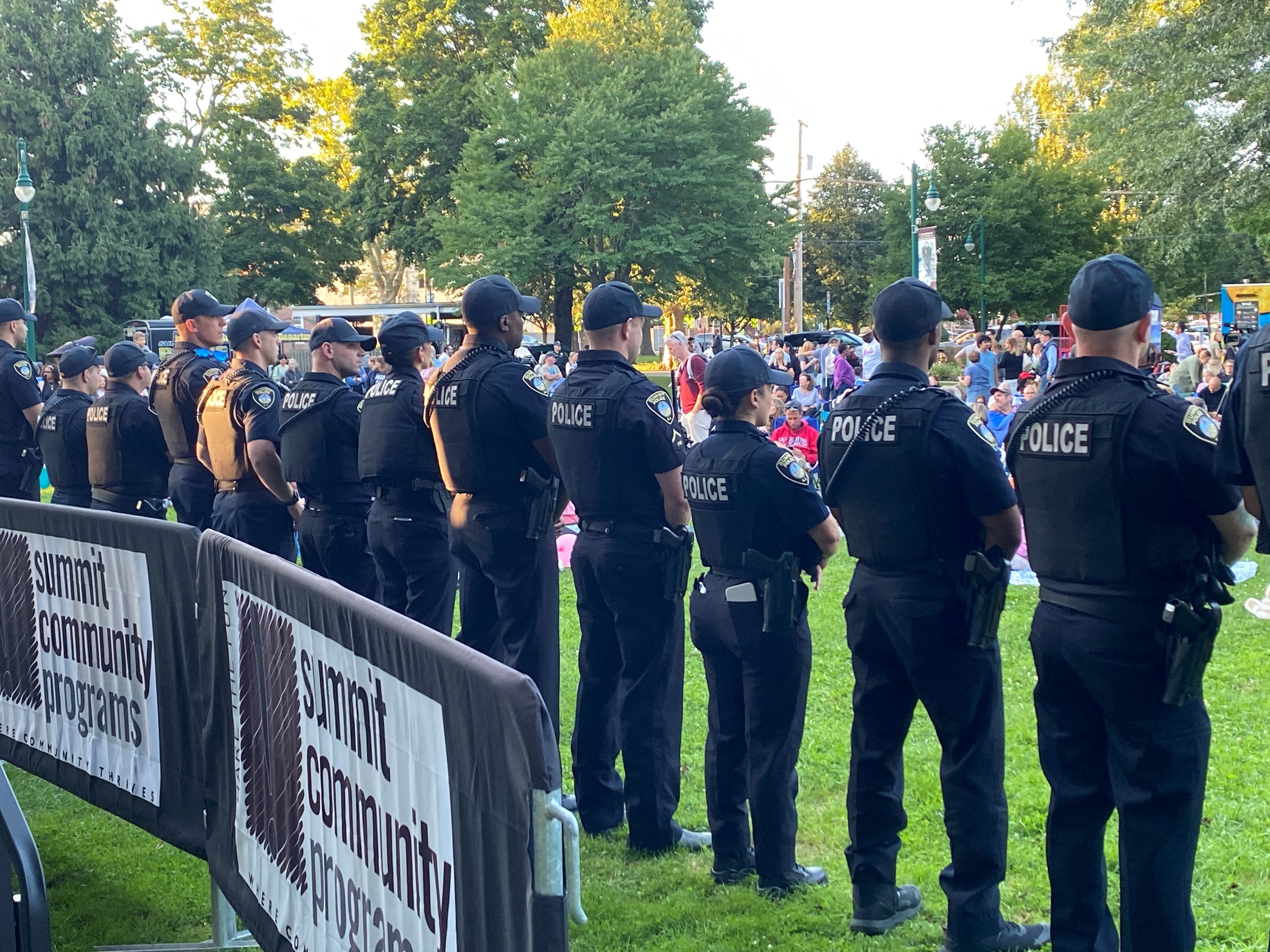 Police officers facing crowd in grassy park area