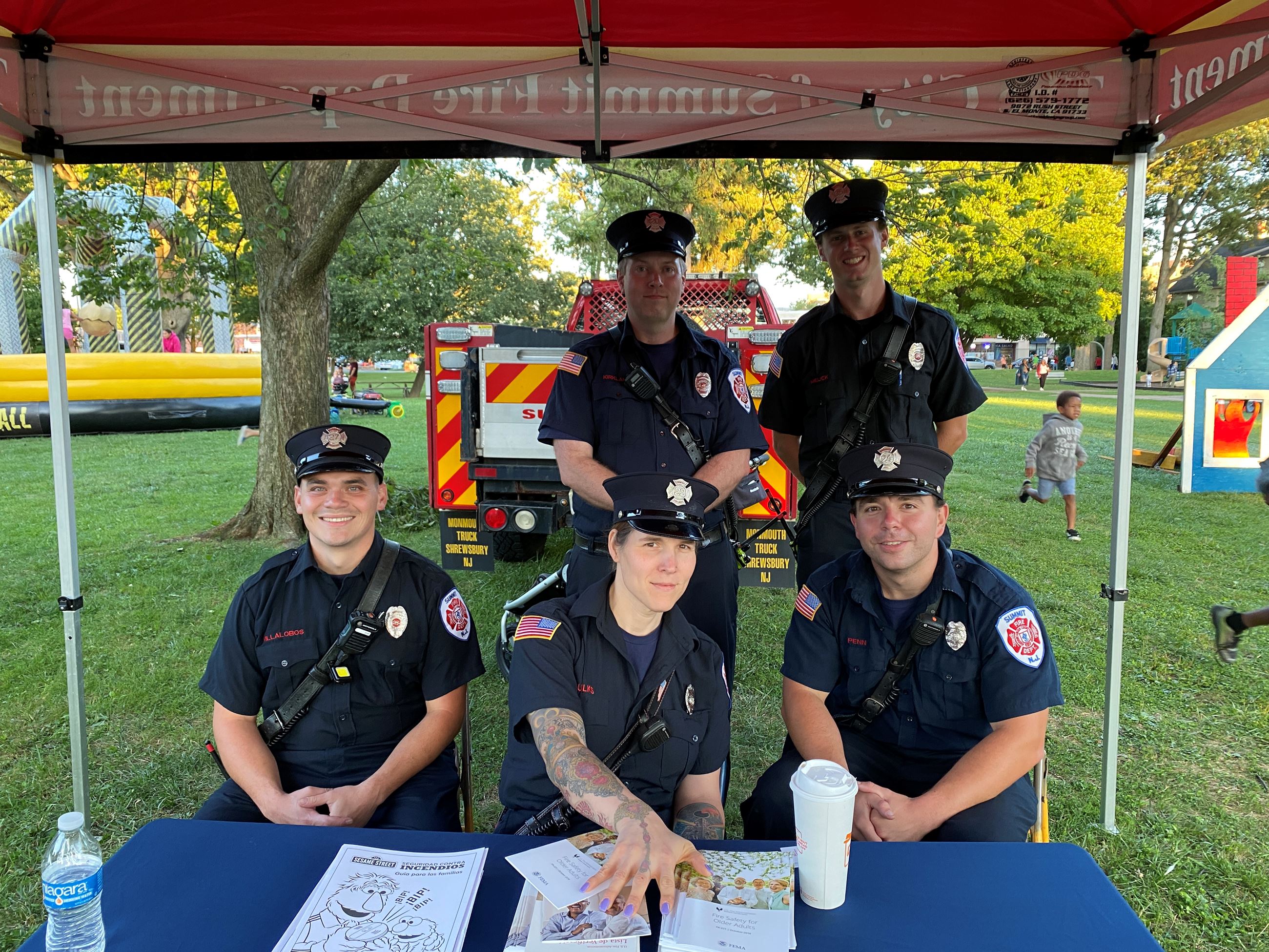 Firefighters seated under tent in park posing for photo