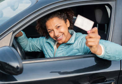 image of woman in the driver's seat of a car holding up a driver's license